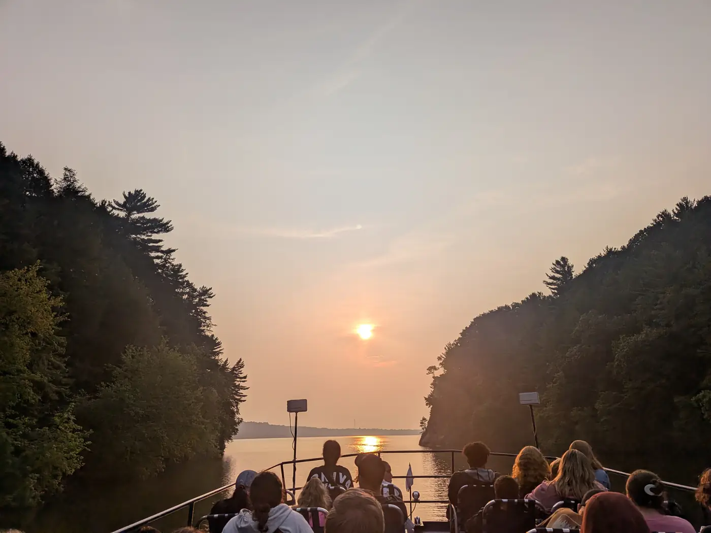 The sun setting between the river bluffs, seen over the boat's passengers